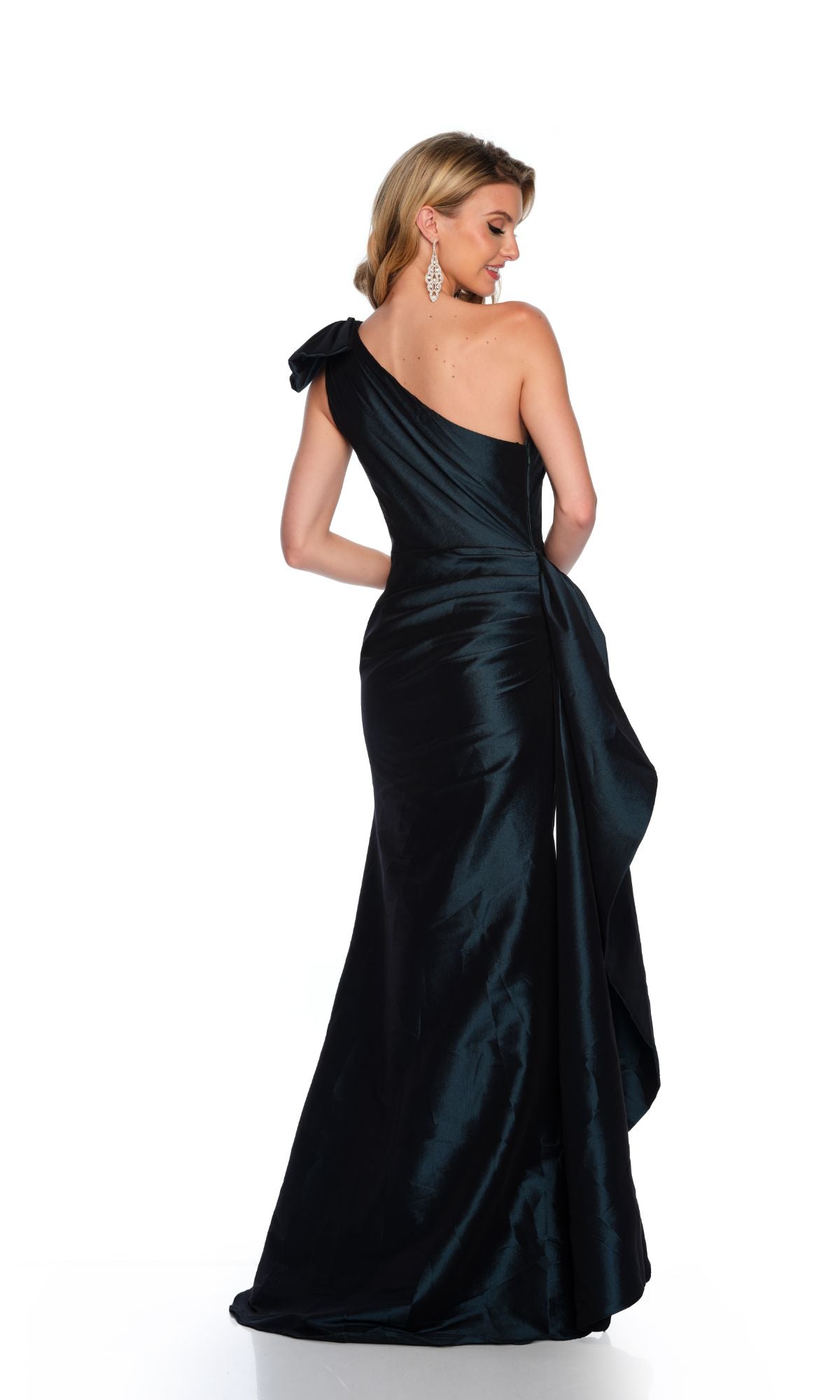 A woman stands facing away in the Long Formal Dress 11598 by Dave and Johnny, showcasing its fitted one-shoulder design, draped back, and elegant side sash against a white background.